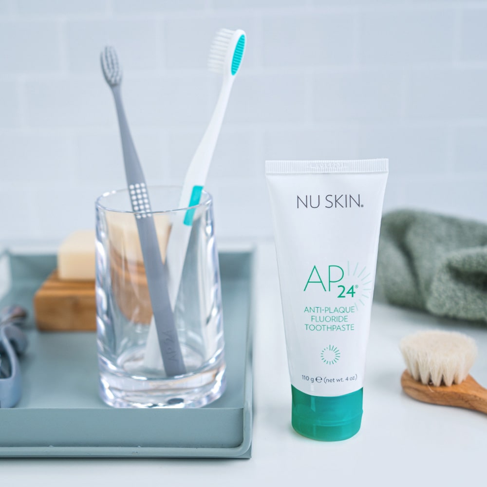 AP 24 Anti-Plaque Fluoride Zahnpasta steht in sanitärer Umgebung neben einem Glas mit Zahnbürsten.