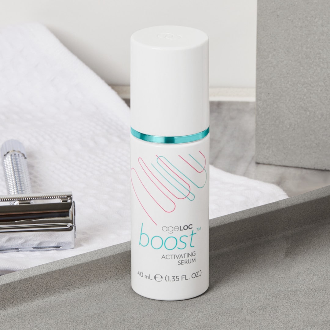 ageLOC Boost Activating Serum von Nu Skin (Dosierspender, je 40ml) steht geschlossen in sanitärer Umgebung vor einem Rasierer und weißen Handtuch.