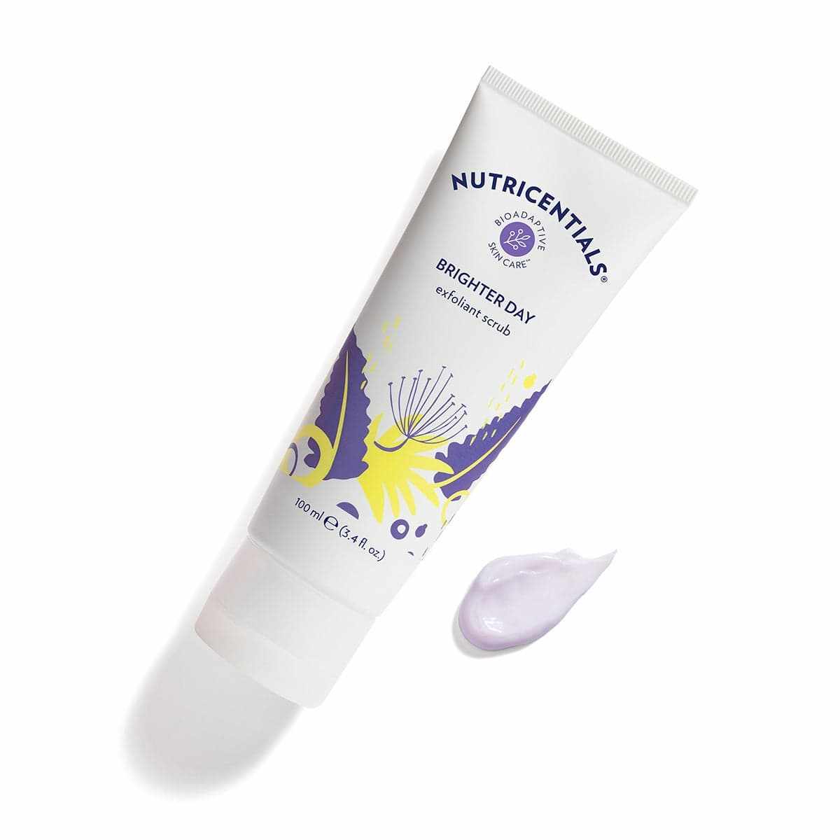 Nutricentials Brighter Day Exfoliant Scrub Tube (100ml) liegt geschlossen auf glatter Oberfläche. Daneben wurde eine kleine Probe des fliederfarbenen Peelings aufgegeben.