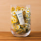 epoch Blemish Treatment Tube (15ml) gut sichtbar in einer mittelgroßen Glasvase. In der Vase befinden sich außerdem eine Menge gelber Blüten Schafgarbe.