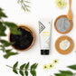 Epoch Yin and Yang Mask, Gesichtstreatment von NuSkin. Tube (75ml) liegt geschlossen auf weißer glatter Oberfläche, umgeben von Blüten und Pflanzenblättern.