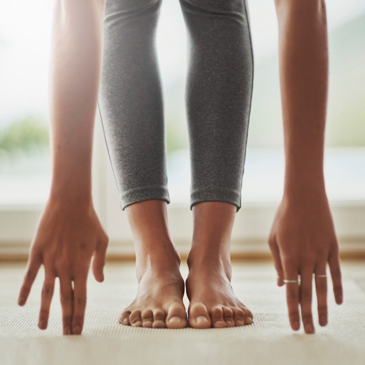 Junge Frau macht Dehnübungen. Ihre Fingerspitzen berühren den Boden, während ihre Beine gerade durchgestreckt sind und ihre Füße vollständig auf dem Boden stehen.