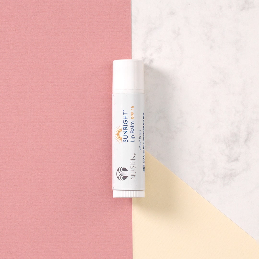 Sunright Lip Balm 15 von NuSkin liegt geschlossen auf pastellrosa/gelben Oberfläche.