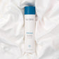 Perennial Intense Body Moisturizer Flasche (250ml) liegt geschlossen in weißen Seidenlaken.