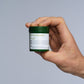 Hand hält geschlossene Pharmanex Pro-B Kapseldose (je 30 Kapseln, Nettogewicht: 10 g) vor hellgrauem Hintergrund.
