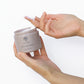 Aus ReNu Hair Mask Behältnis (100g) wird vor weißem Hintergrund mit den Fingerspitzen eine kleine Probe entnommen.