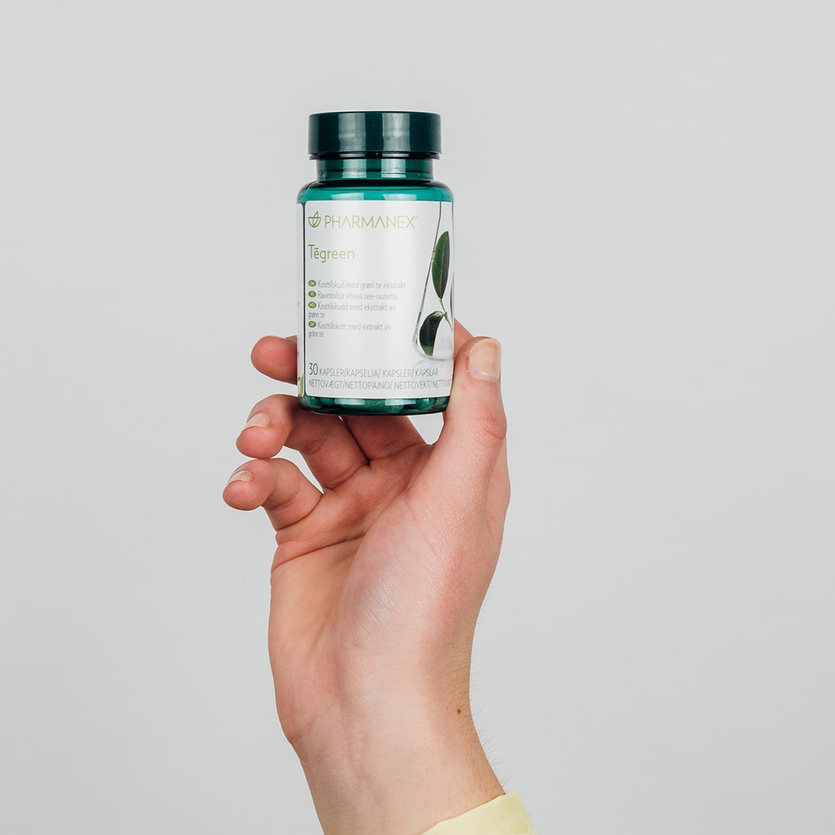 Hand hält Pharmanex Tegreen Kapselglas (30 Kapseln) in die Höhe.